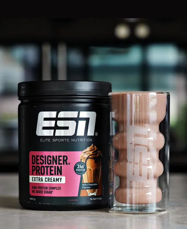 ESN Designer Protein Extra Creamy – Milk Chocolate, con un bicchiere